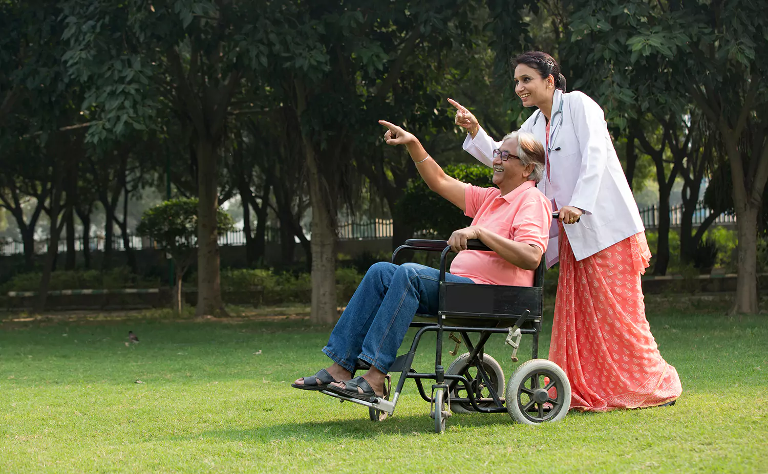 Disabled man in a wheelchair with his doctor on the garden pointing together at something